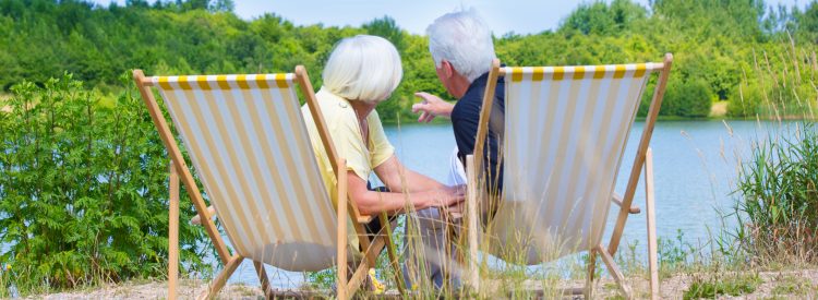 Retired couple sat by lake on deckchairs. Viewed from the back.