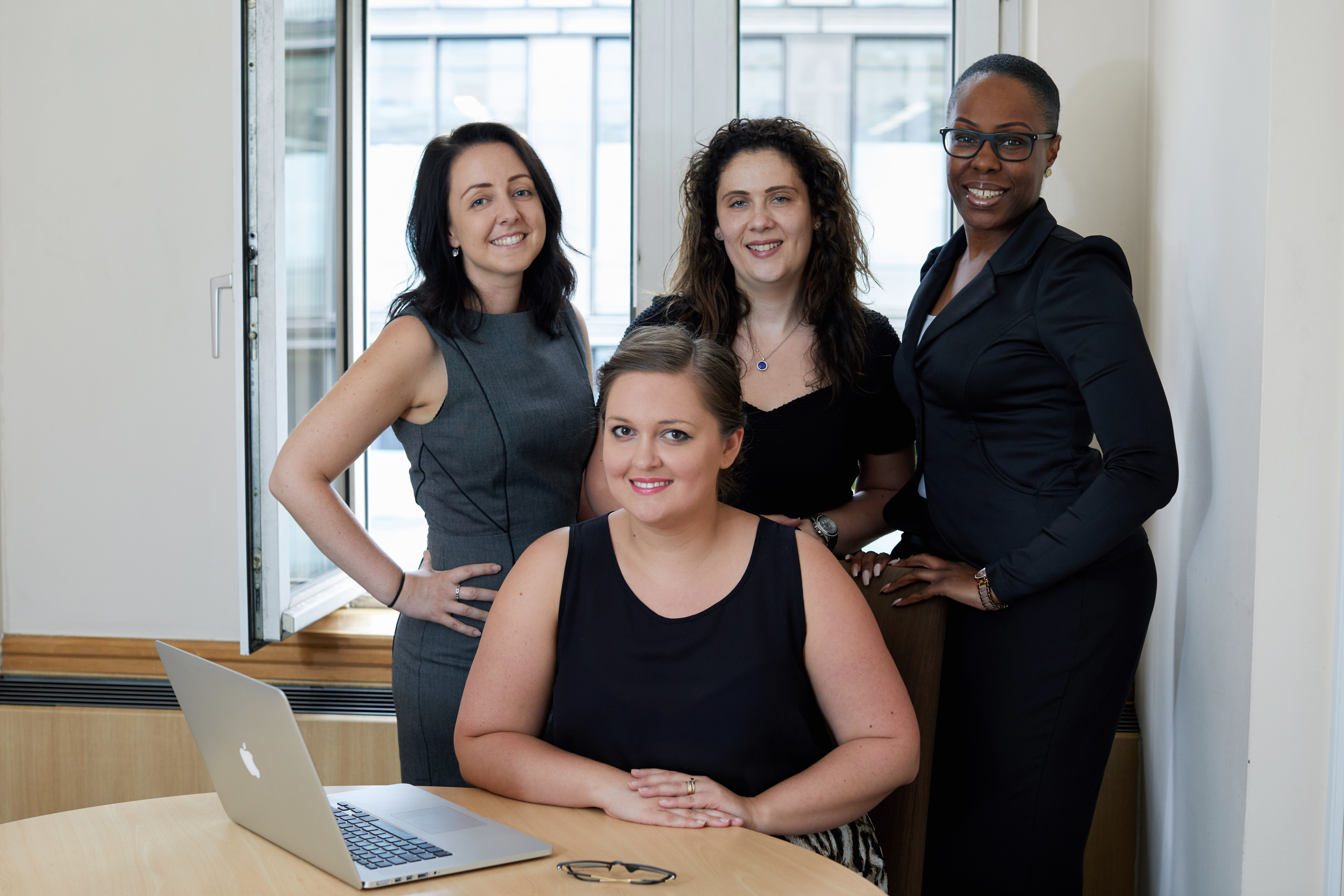 4 female office staff stood behind desk