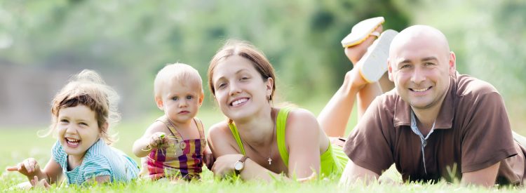 Happy family of four enjoying time at grass in summer park