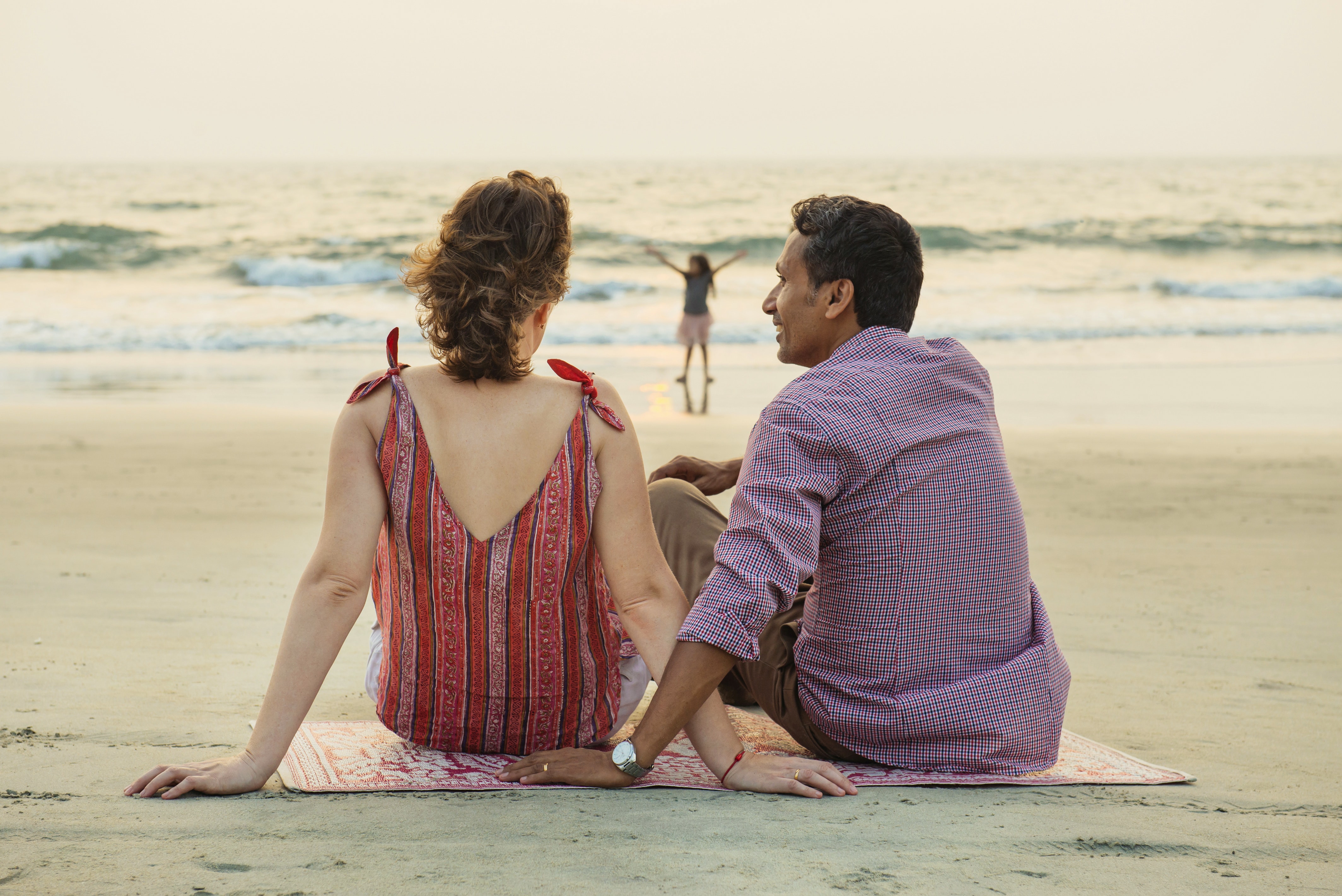 Couple relaxing on beach, looking out to sea